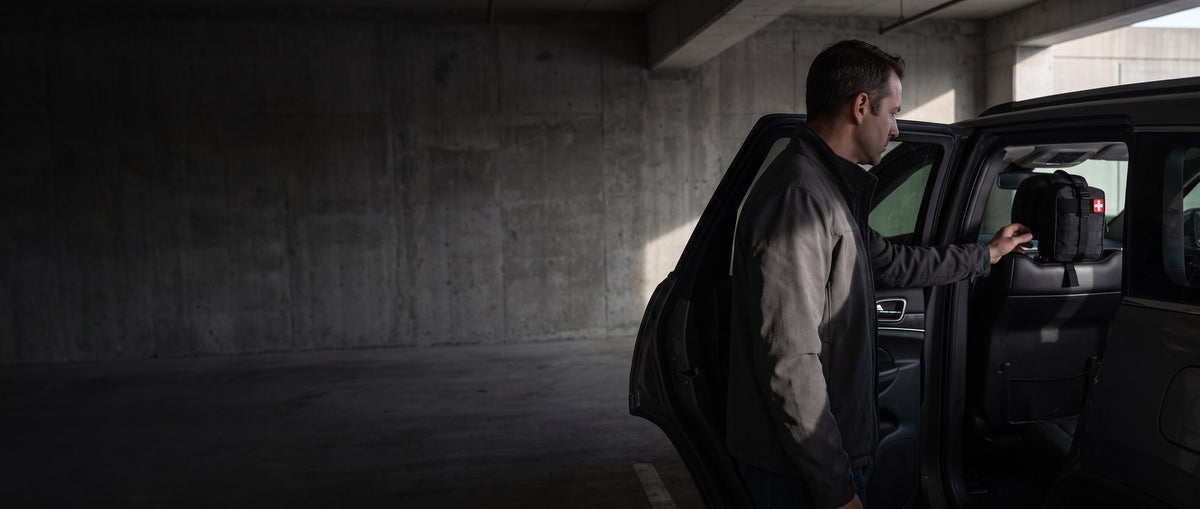 Man at an open SUV door in a parking garage reaching for a first-aid kit strapped to the headrest